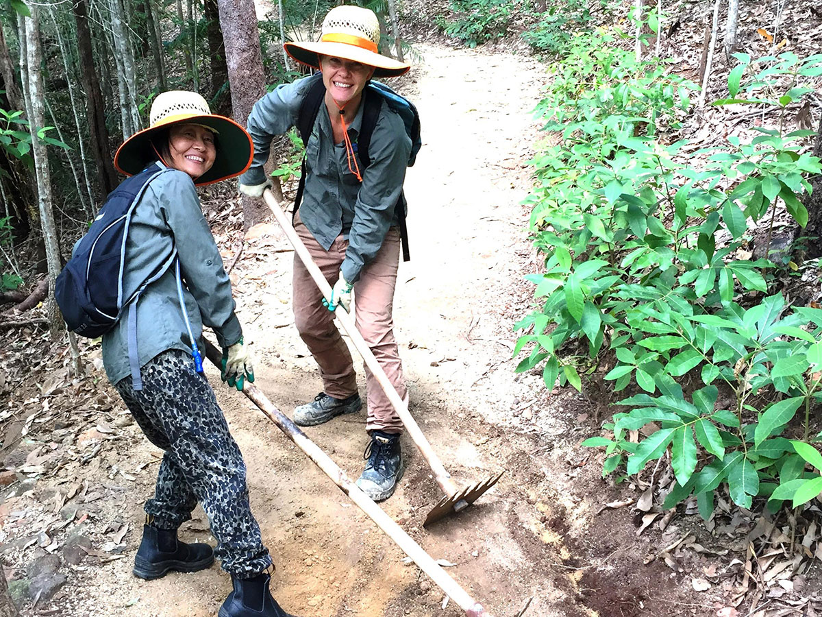 Two female volunteers use rakes to smooth new dirt surface on Arrow Trail