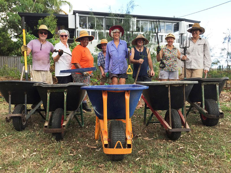 Group of eight community members post with wheelbarrows and tools at their local park