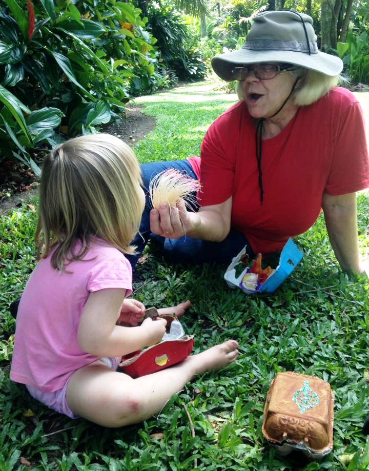 Volunteer sitting on ground showing young girl a feather found in the Cairns Botanic Gardens