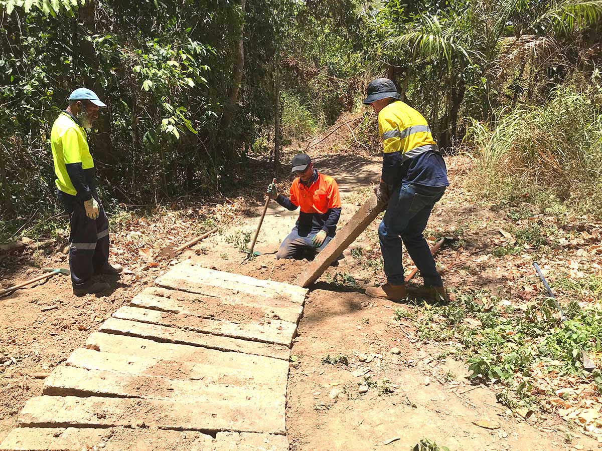 Three volunteers placing new wooden plank on walkway under construction