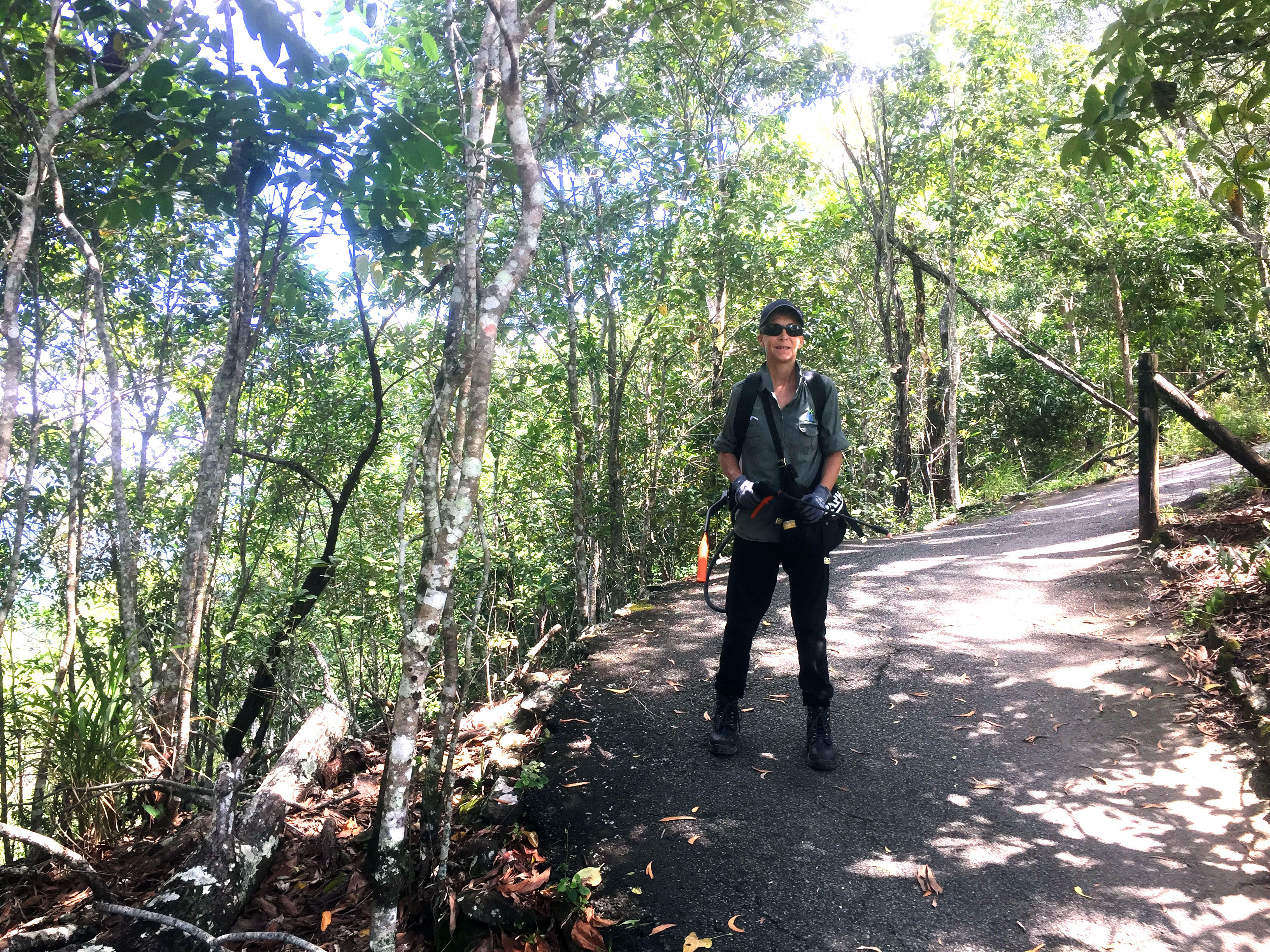Woman stands on steep path with weed spray gun in hand