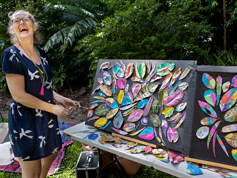 Woman laughing next to display of colourful leaves painted by children