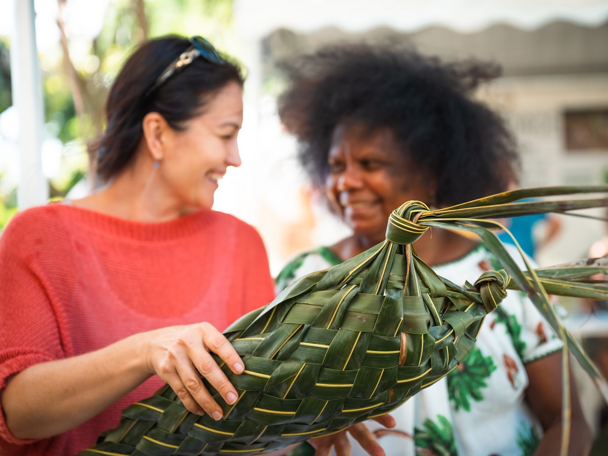 One woman shows another woman a basket woven from coconut frond.