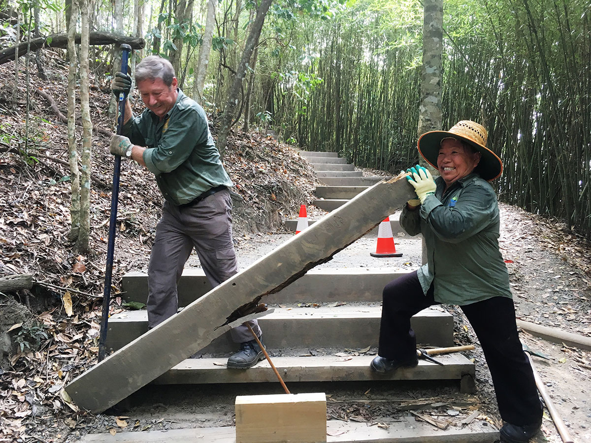 Volunteer using a crow bar to place new pre-cast step being held by second volunteer