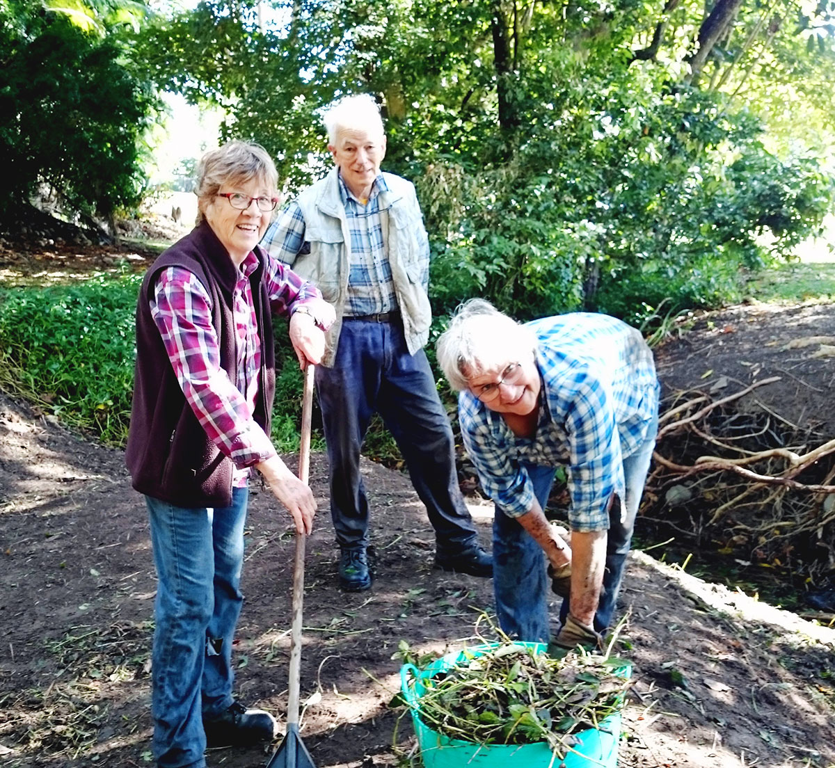 Three community members with tools and bucket of weeds removed from local park
