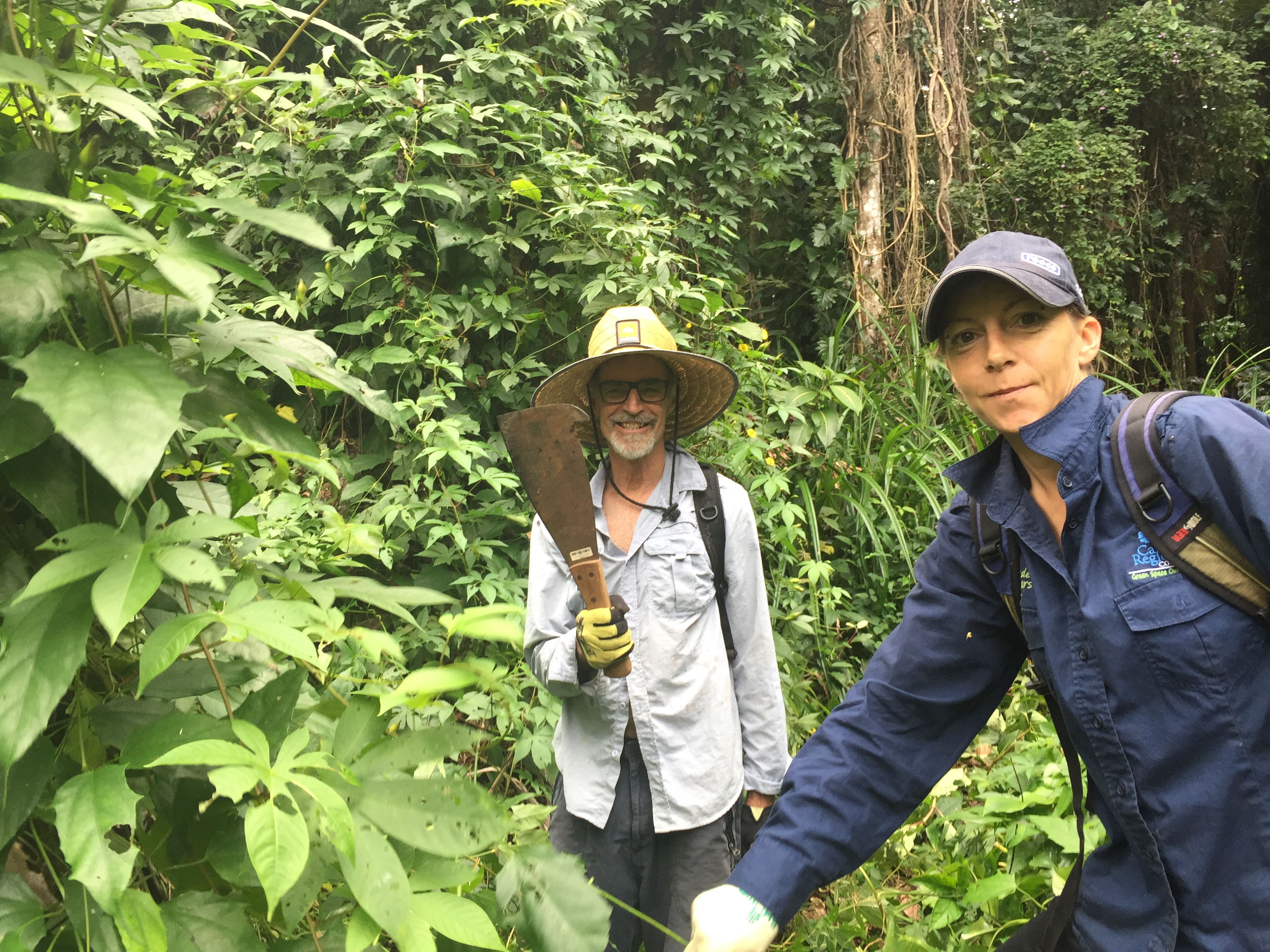 Man holding machete and woman among overgrown invasive weeds