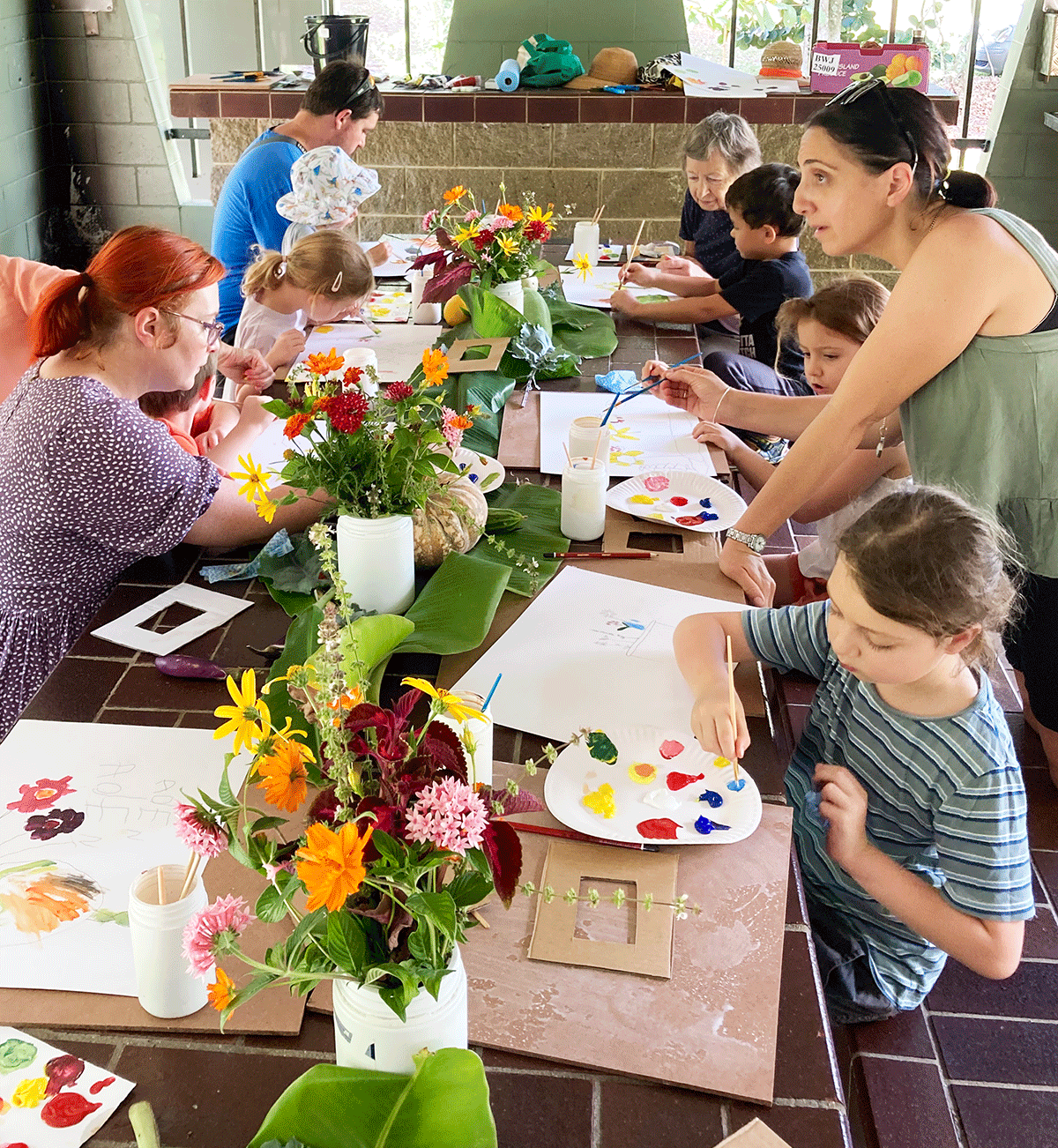 Children and parents painting at large table with vases of flowers as inspiration