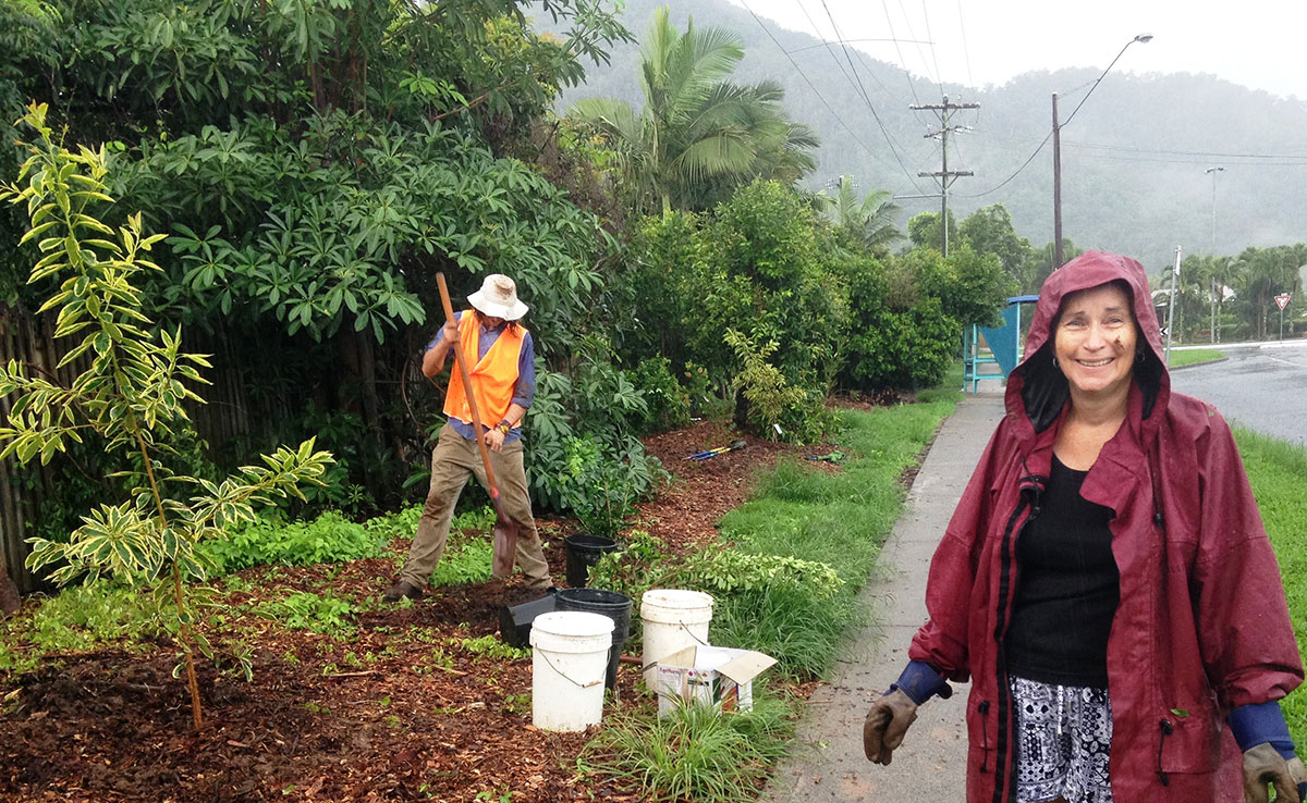 Man in background mulching road verge with woman in raincoat in foreground
