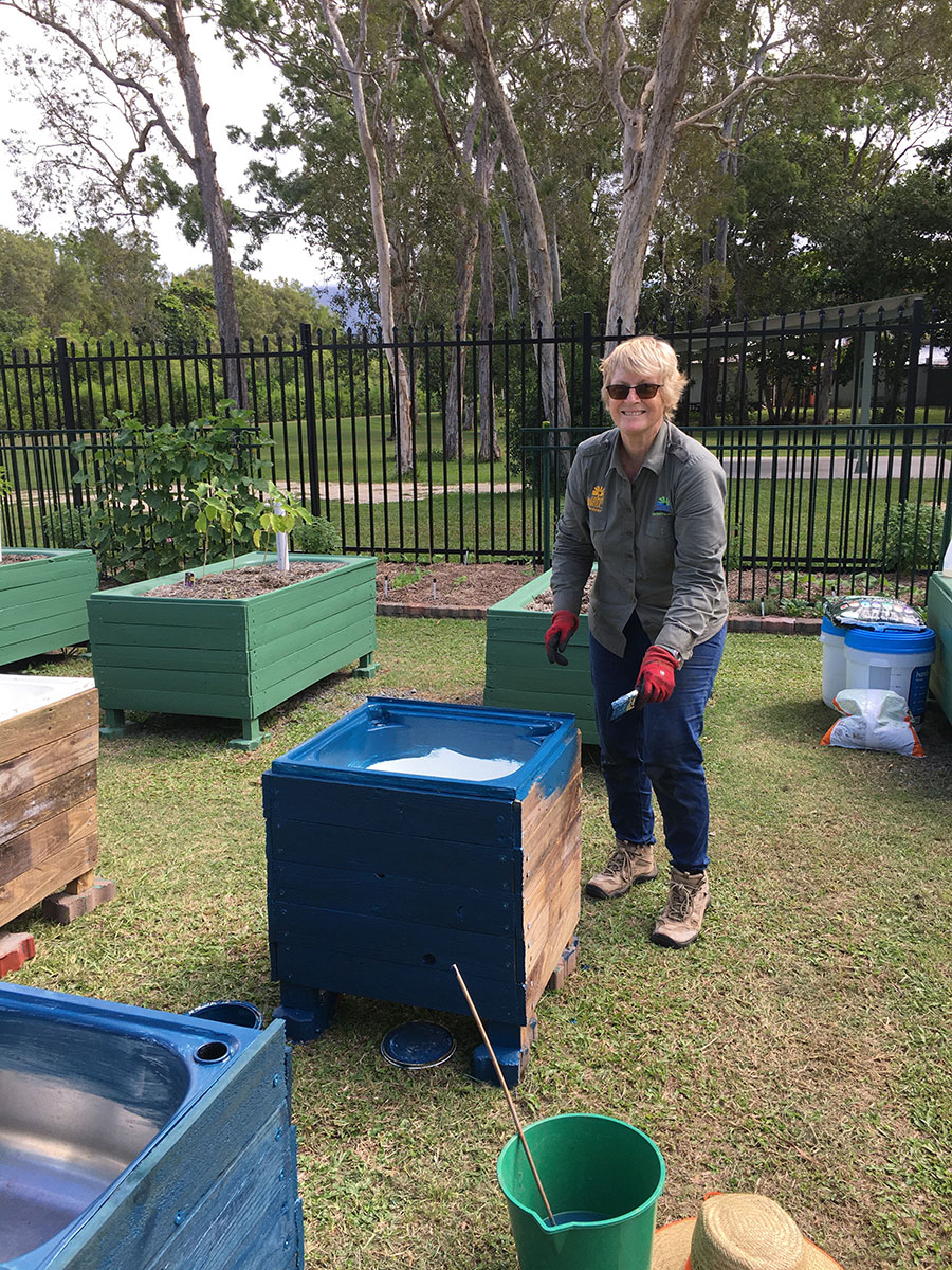 A volunteer paints the outside of a new wicking bed made from an older kitchen sink