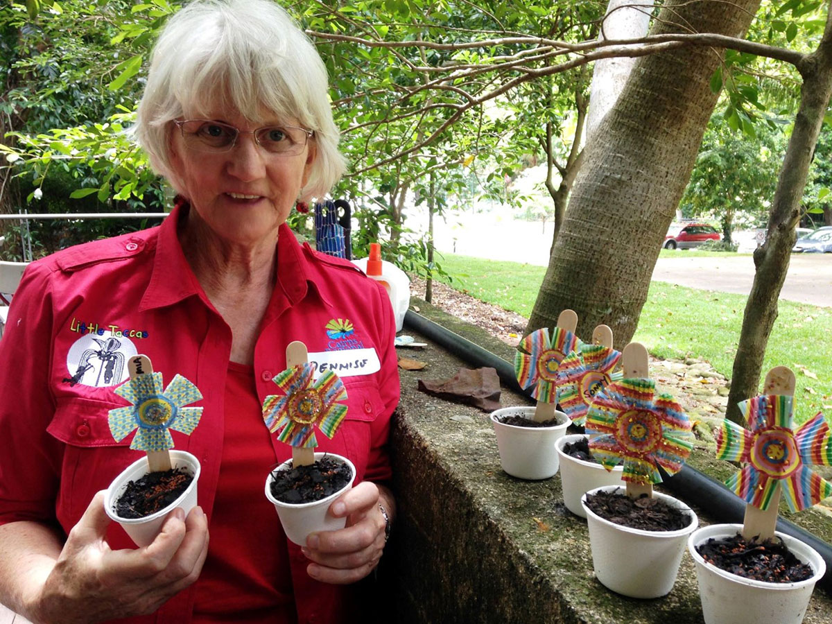 Volunteer holding two pots with decorated sticks indicating type of planted seeds