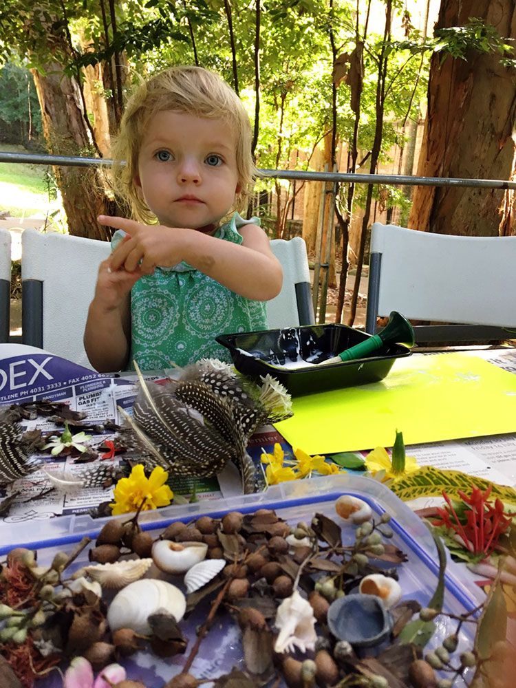 Young girl with feathers, shells, twigs, flowers and other found objects during collage session
